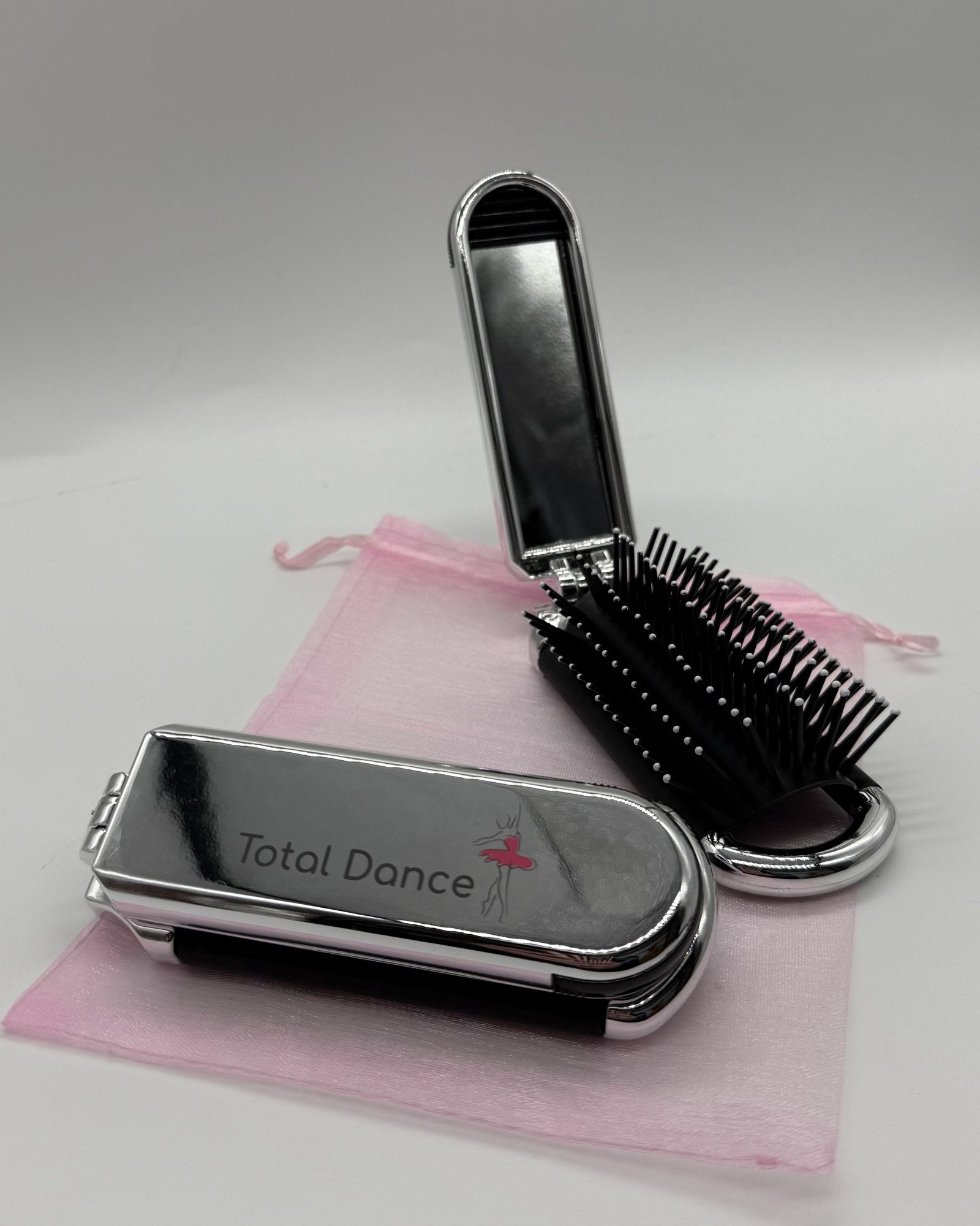 Total Dance foldable hair brush open showing the removable mirror and cushioned bristles beside the folded compact with pink organza pouch